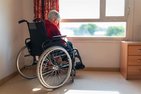 An older woman with white hair, alone in her house while looking outside through the window waiting for company.