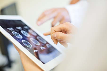Close up of doctors hands pointing at brain xrays images on digital tablet.